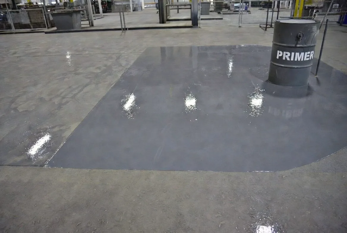 Endüstriyel beton zeminde primer uygulanmış yüzey bölümü ve primer varili